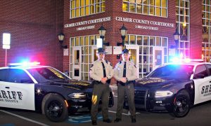 Photo of two Gilmertt County Sheriffs standing in front of their patrol cars